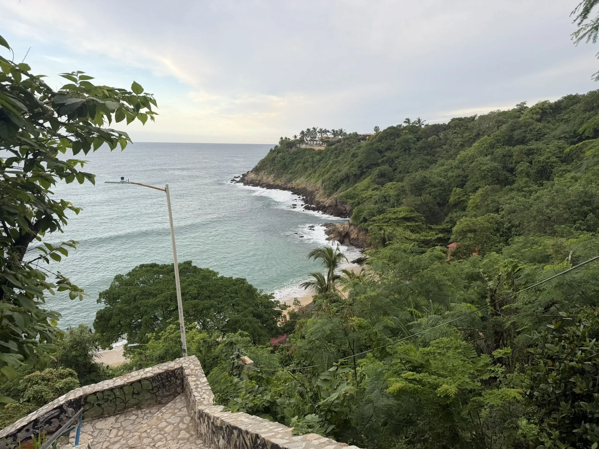 A small bay in Puerto Escondido seen from above, between the sea and hills covered in green forest
