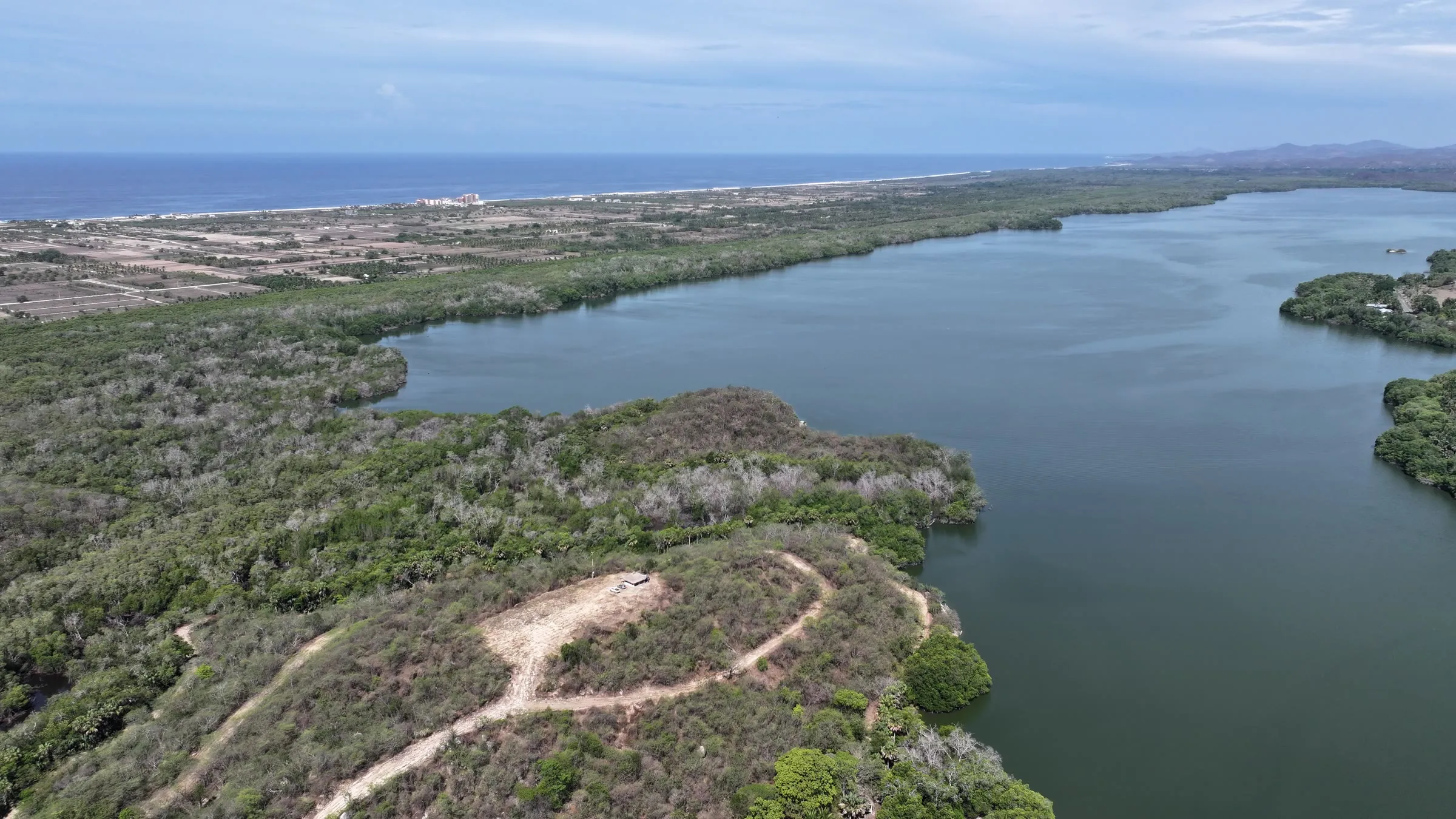 Aerial view of a coastal lagoon surrounded by dry forest, with the Pacific Ocean on the horizon