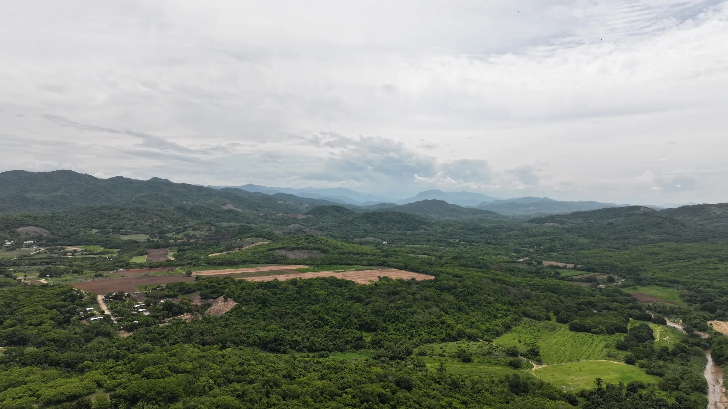 Aerial view of a green valley with fields, a small village and mountains under a cloudy sky